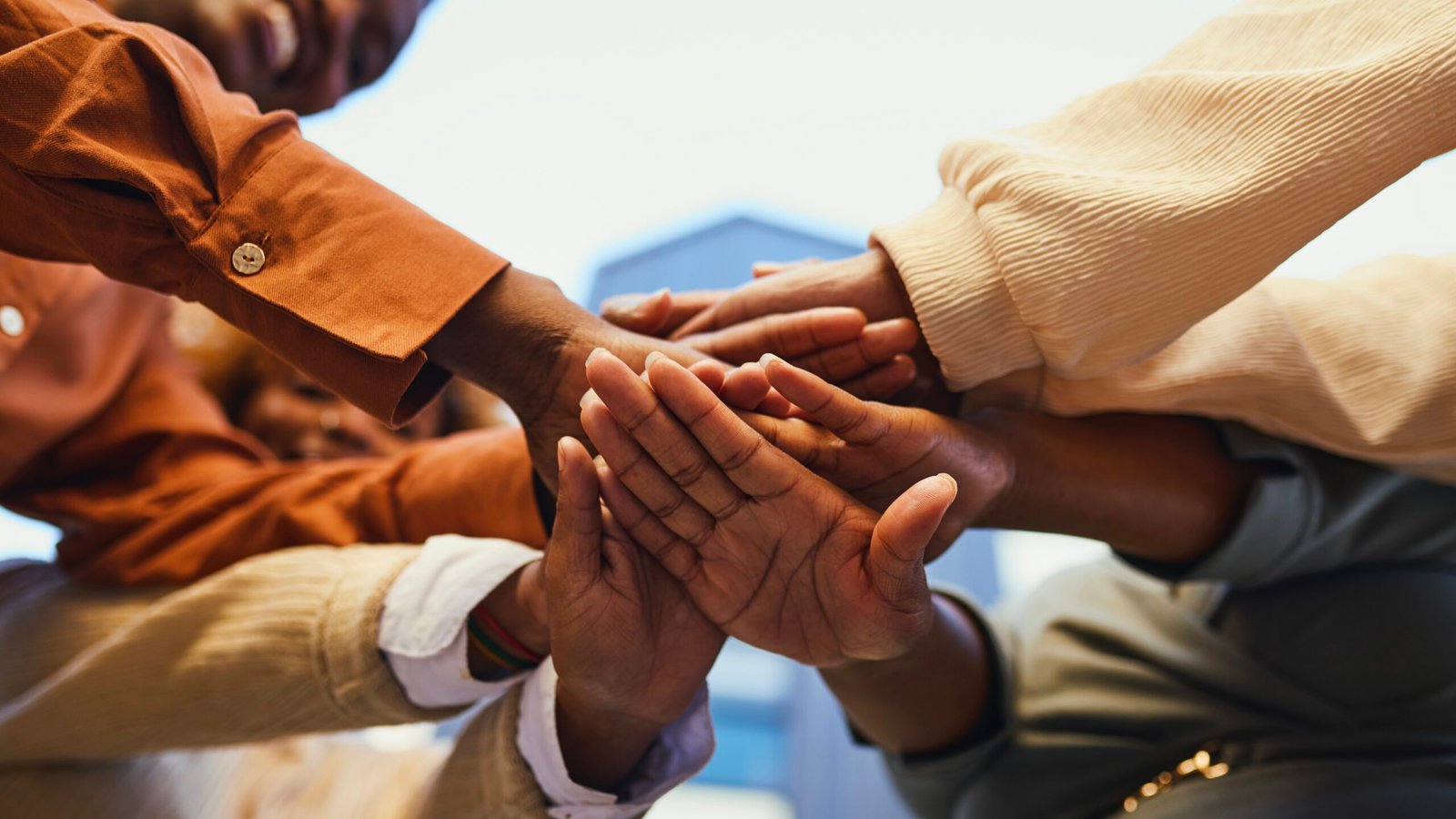 Close-up worm's eye view of best friends stacking hands in unity outdoors Best friends wearing smart casual attire gathering in circle and stacking hands, celebrating friendship and unity, bonding outdoors