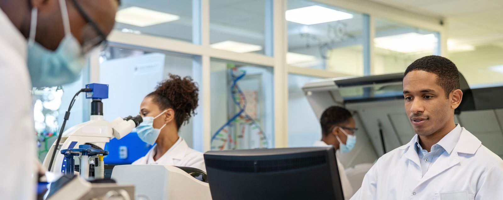 Male scientist working on computer with colleagues working around in lab. Group of people working in a science laboratory.